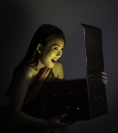 Young woman excitedly opens mysterious box as glowing contents shine on her face