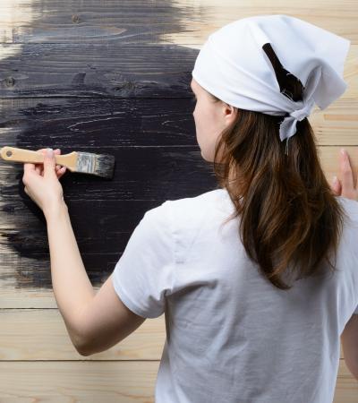 Teenage girl wearing white shirt and headscarf paints wooden wall black