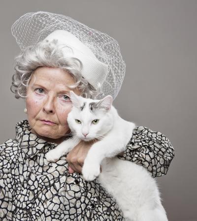 Eccentric senior lady wearing vintage hat poses with her cat