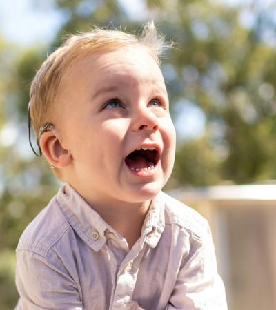 Photograph of a toddler with a hearing aid smiling up.