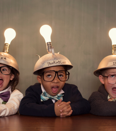 Photograph of three children dressed in smart clothing with caps and lit up lightbulbs on their heads.
