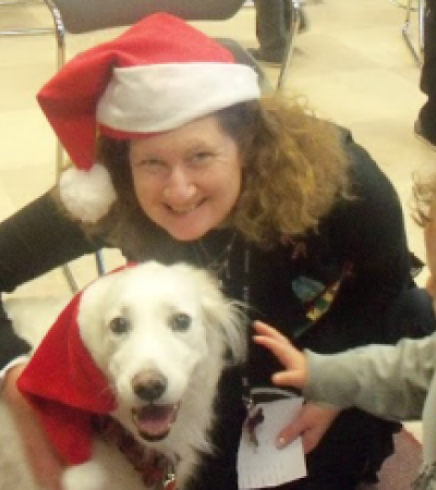 A woman wearing a Santa hat and a child pet a dog