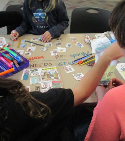 Photograph of kids working at a table with art supplies to create their Needs and Wants project