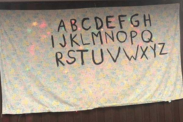 Alphabet letters painted on a sheet with Christmas lights behind the sheet