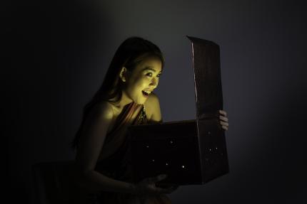 Young woman excitedly opens mysterious box as glowing contents shine on her face