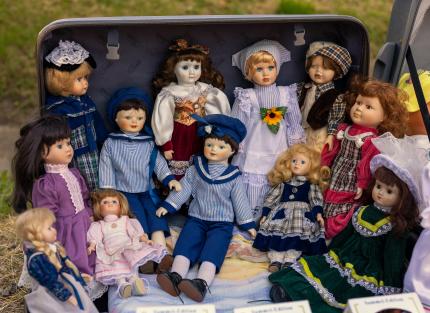 A veritable crowd of elegantly-dressed dolls sit and stand in a suitcase