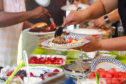 photo focused on hands filling plates over an array of potluck dishes