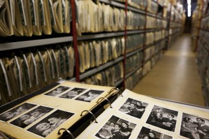family photos in the foreground and family history files run the length of the aisles at the genealogy library