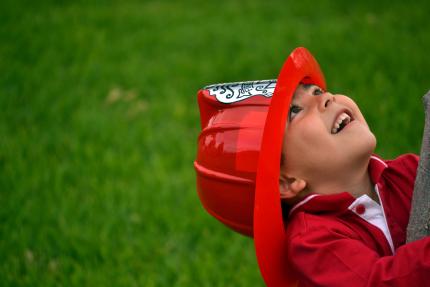 happy little boy wearing plastic fire helmet on grassy background
