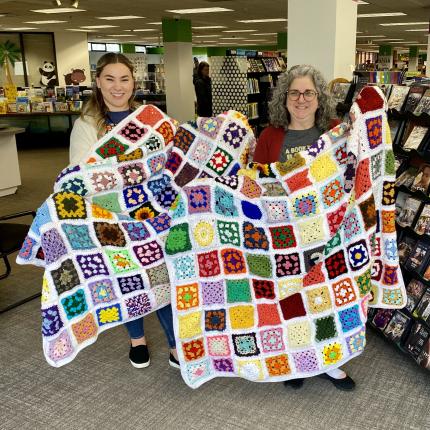 Photograph of two people smiling holding up finish granny square blankets