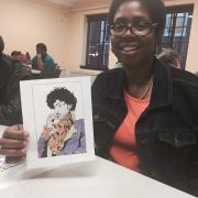 A woman smiles and shows off a photo of Prince that she colored.