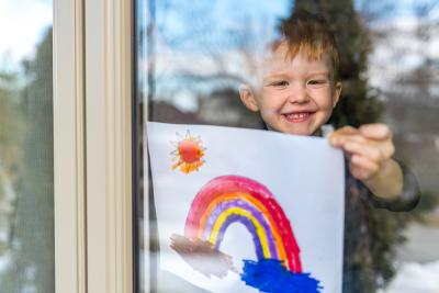 A child hanging a painting of a rainbow inside a window
