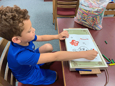Young boy applying a crayon to a drawing over a hot plate