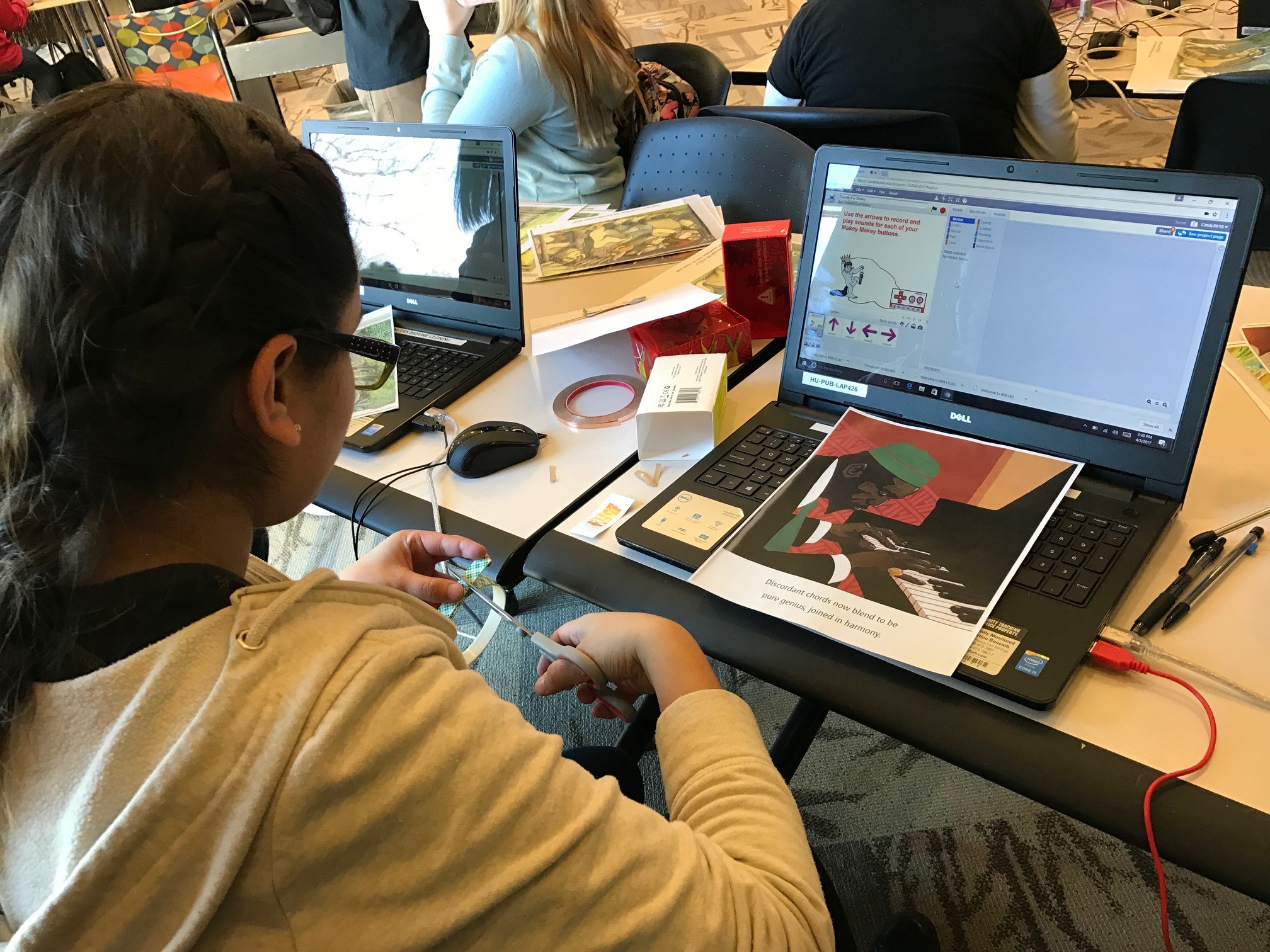 Photograph of a teen working on creating a tactile book, they are cutting out designs in front of an open laptop.
