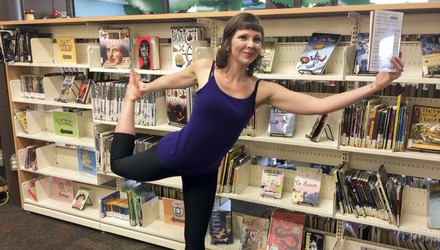 Woman holds a book while balancing in dancer pose at the Fredericton Public Library