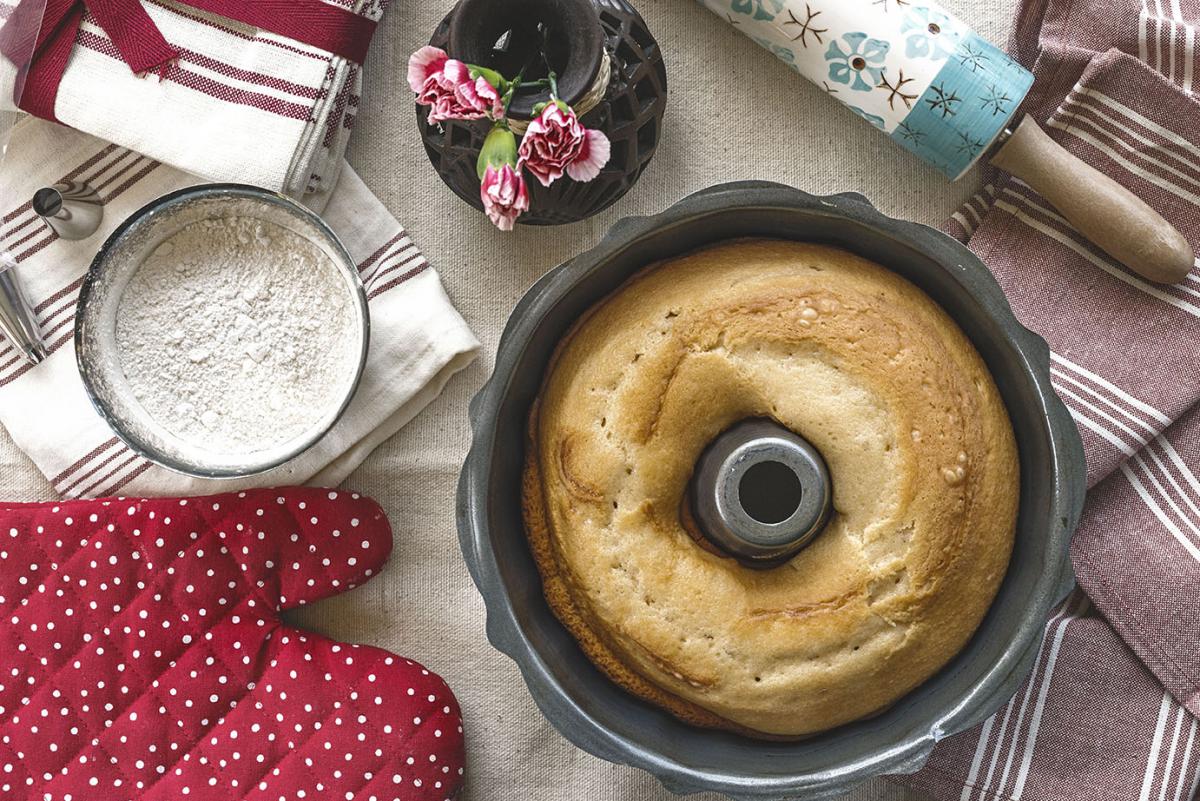Bundt cake in a pan with flour and oven mitts laying next to it.