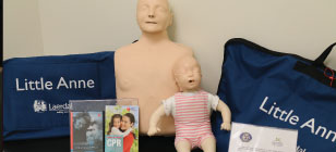 Two tolls sit on a table with bags and instruction books for how to perform CPR.