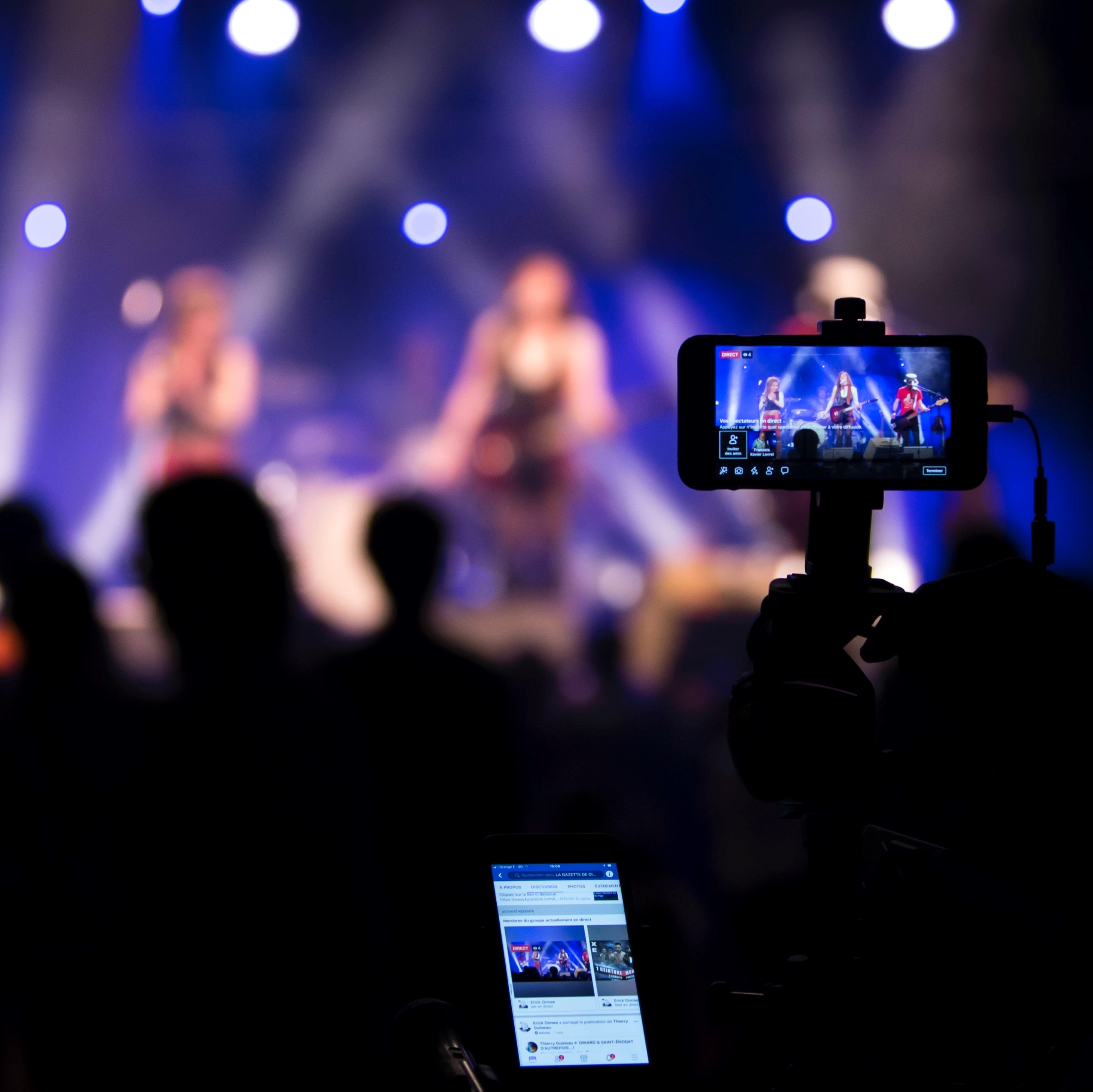 Photograph shows a concert being livestreamed on a camera and phone.
