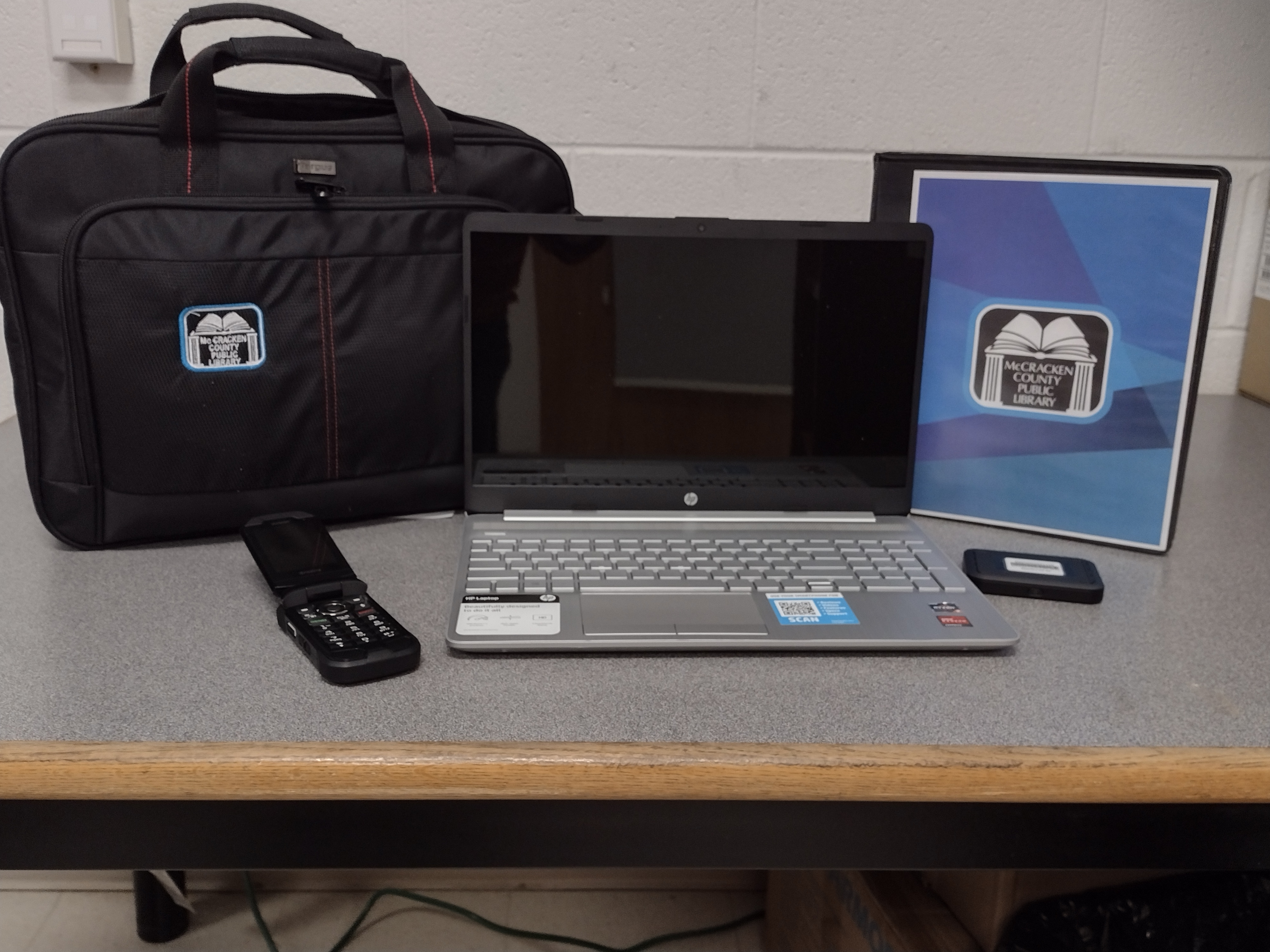 Photograph of the toolkit. Photo shows a black bag, Chrome book, cell phone, flash drive and folder of resources.