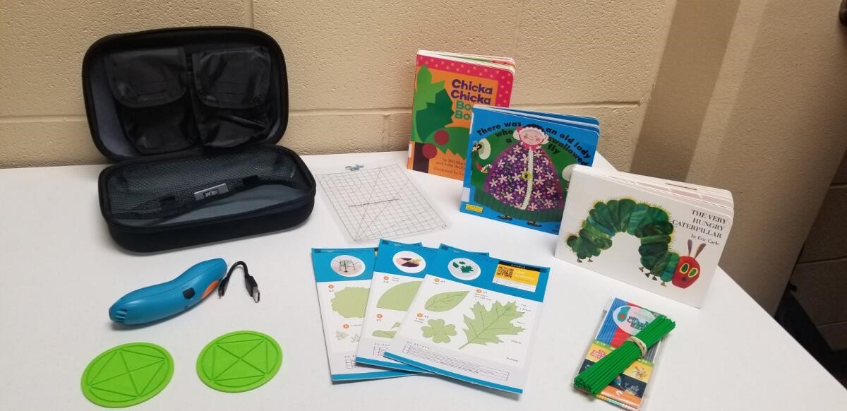 Photograph of a Build a Better Book kit at Laredo Public Library. There are two board books, a 3d pen, filament and tracing stencils 