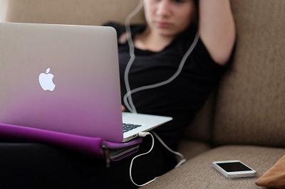 Teenage girl with headphones on looking at her laptop.