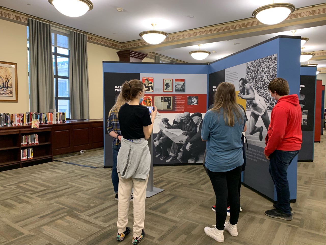 Photograph of a group of people looking at the Americans and the Holocaust exhibition panel inside of Penn State library.