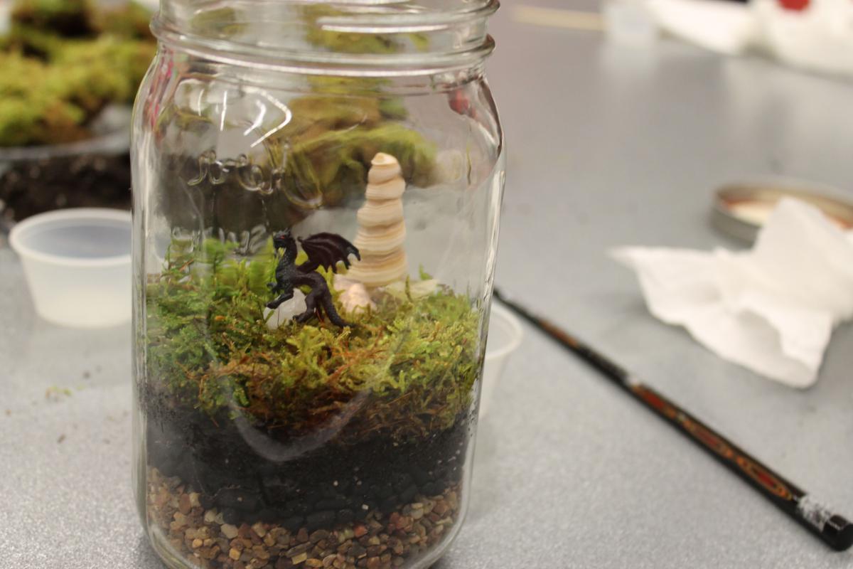 An Earth Day terrarium with a toy dragon is on a table.