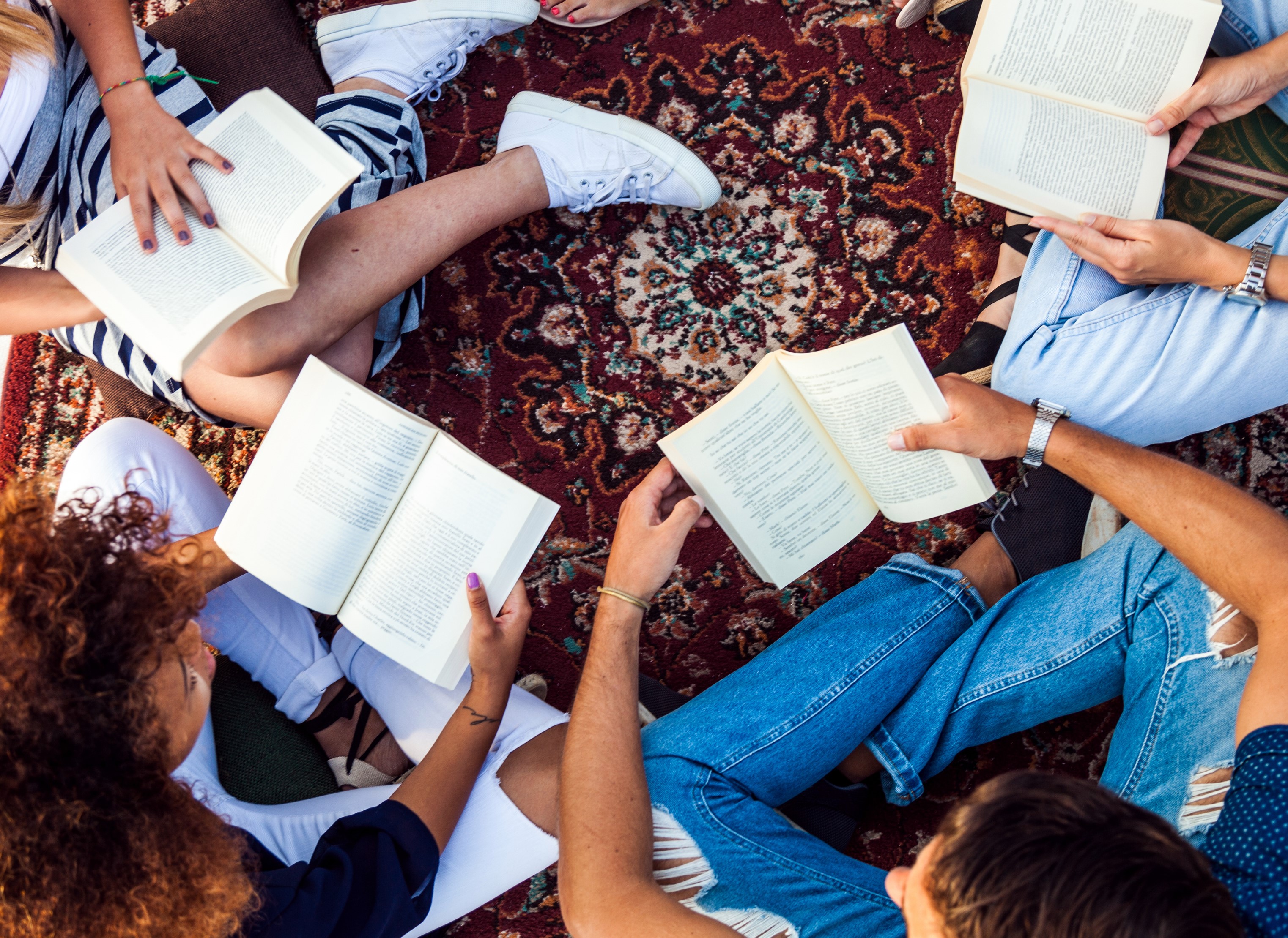 Photograph shows aerial image of four people sitting in a circle with books open in their laps.