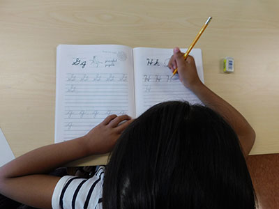 A girl practices writing the letter H in a cursive practice workbook