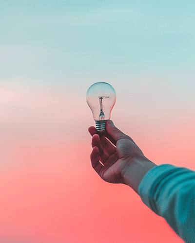 Hand holding a lightbulb against a pink and blue sky