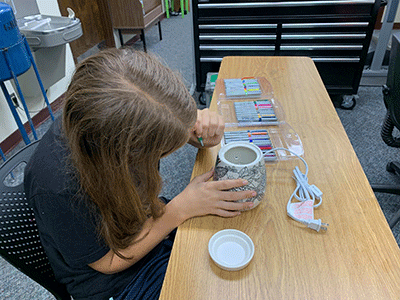 A child coloring a Scentsy pot with markers at a table.