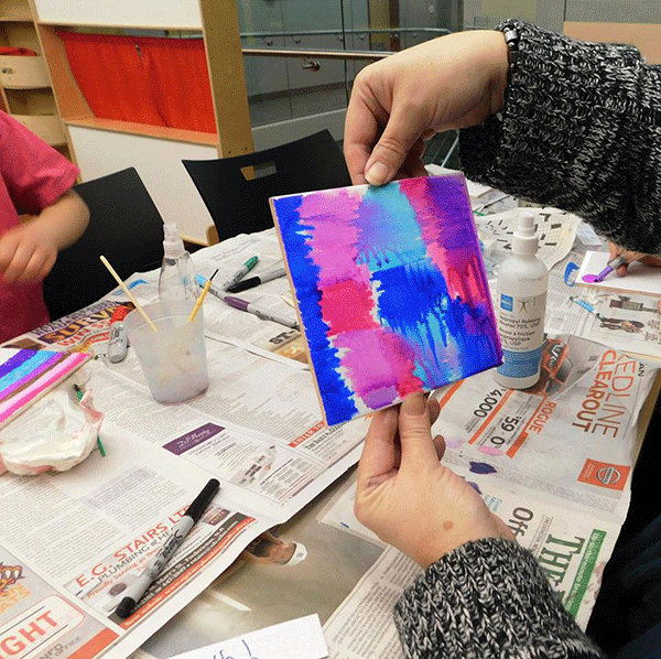 A program participant holds up their finished tile art project