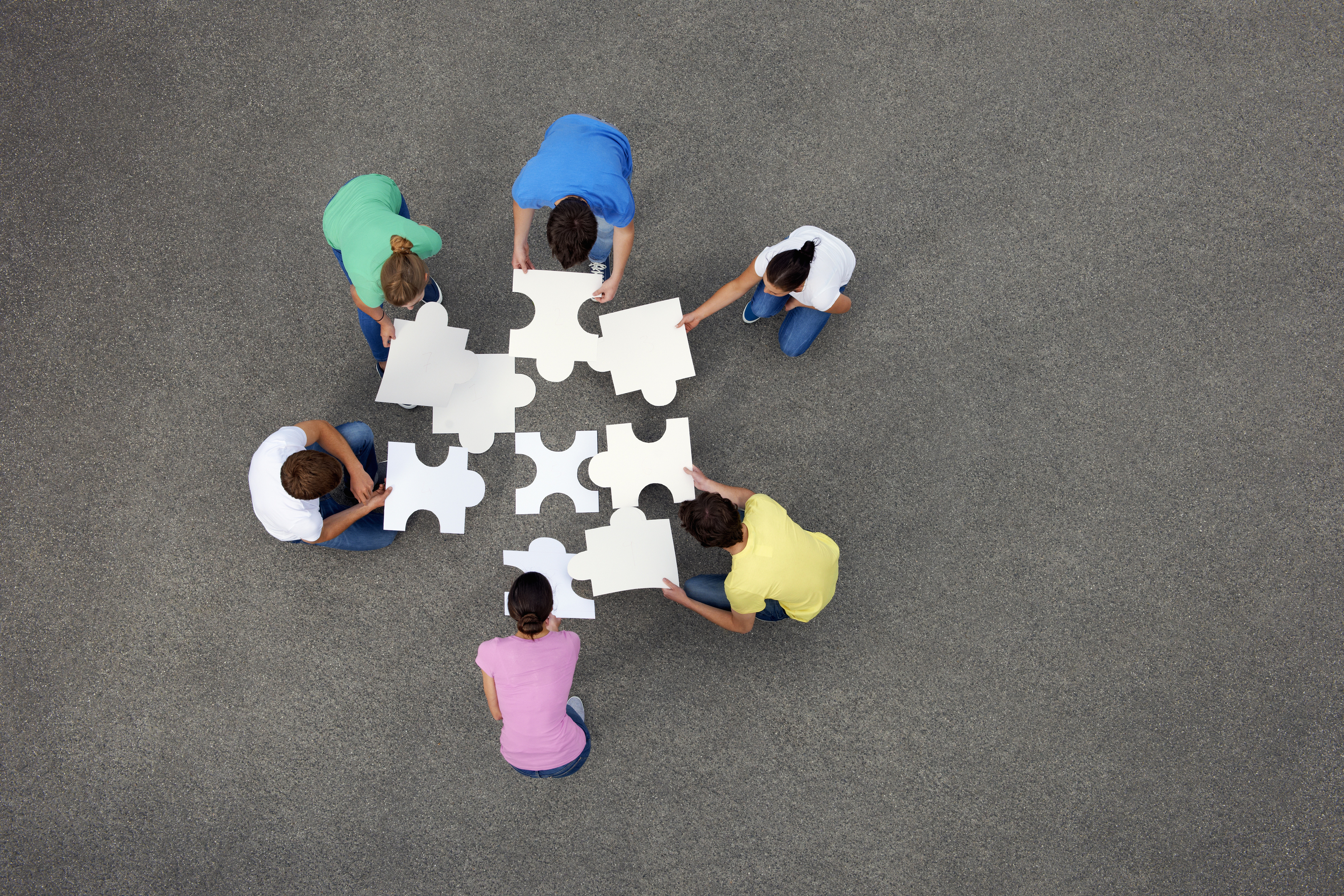 Aerial photograph of six people putting together a large jigsaw puzzle.