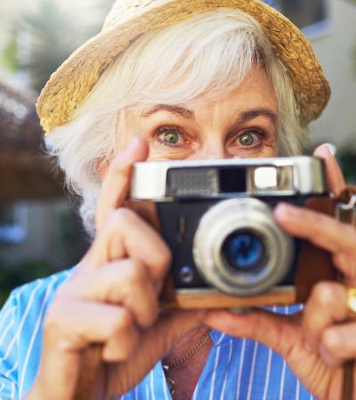 senior lady with straw hat and smiling eyes getting ready to snap a picture with her digital camera