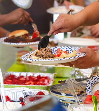 photo focused on hands filling plates over an array of potluck dishes