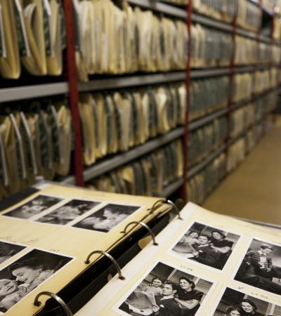 family photos in the foreground and family history files run the length of the aisles at the genealogy library