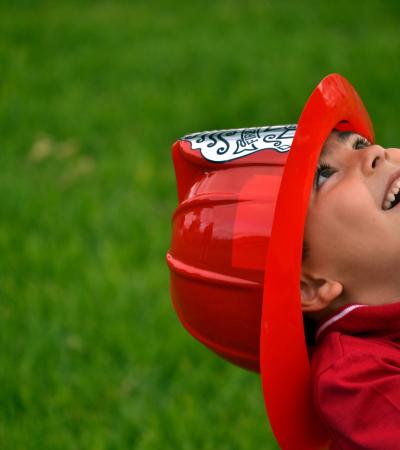 happy little boy wearing plastic fire helmet on grassy background