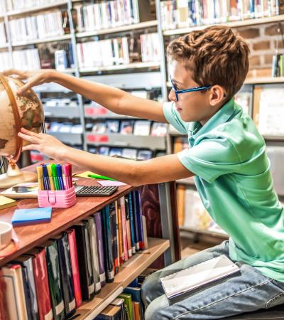 schoolboy studying in the library using a globe