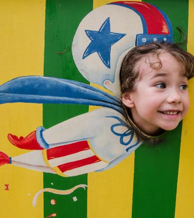 little girl pretending to fly like a cannon ball out of a cannon using a face-cutout at a circus