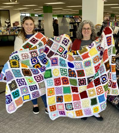 Photograph of two people smiling holding up finish granny square blankets