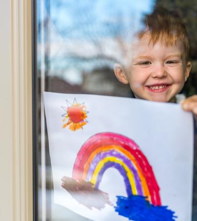 A child hanging a painting of a rainbow on the inside of a window