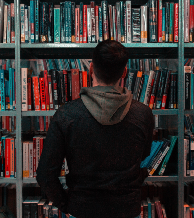 Photograph of a person with their back to the camera, facing a large bookshelf.