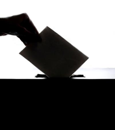 Silhouetted photo of a hand placing a ballot into a ballot box.