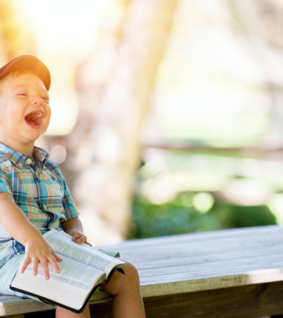 Photograph of smiling child sitting on a bench holding an open book