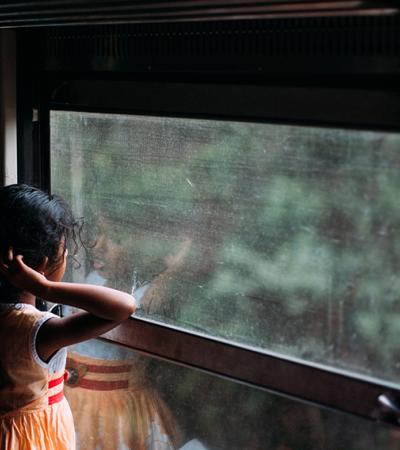 A shadowy photo of a young girl looking out a window at some trees