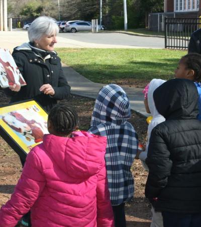 Photograph of librarian reading a story during a StoryWalk to a group of children.