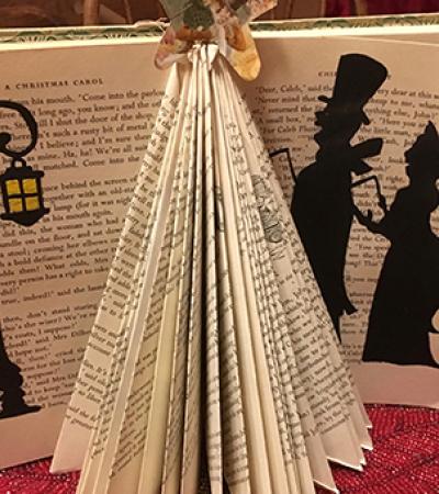 Book standing up open with the pages folded to form a triangle fan with black paper cut and pasted to the open pages to look like two people walking by a street lamp.