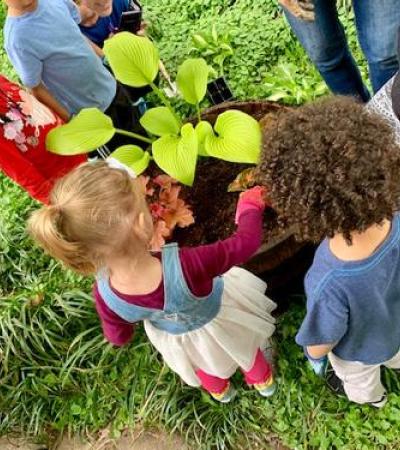 A group of kids outdoors standing around a plant