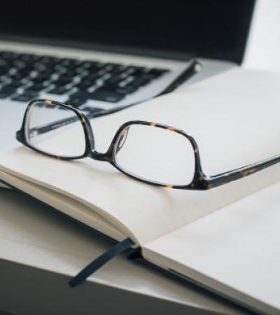 a laptop, eyeglasses, open notebook on a desk