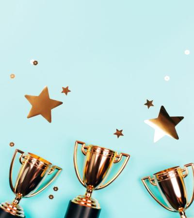 Photograph of gold trophies against a blue background with stars.